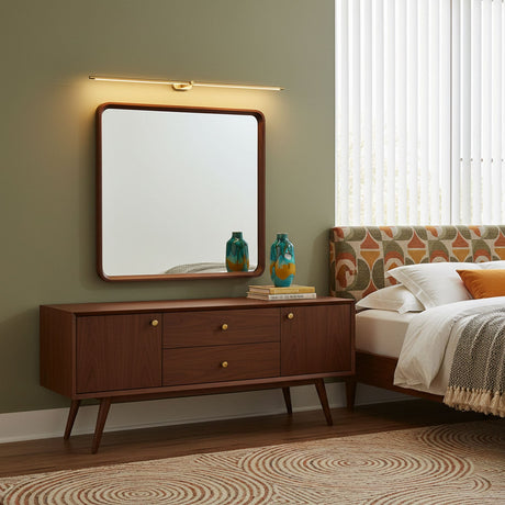 Slim rod lit above a framed mirror over a walnut sideboard in a green bedroom
