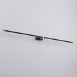 The black and gold rod seen at an angle, a thin line against a pale wall
