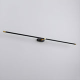 The black and gold rod seen at an angle, a thin line against a pale wall