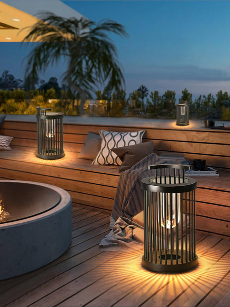 Two lanterns lit on a timber deck beside a concrete fire bowl and cushions