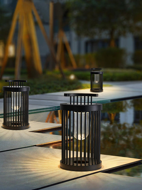 Two lanterns lit on a paved garden walkway with planting behind them