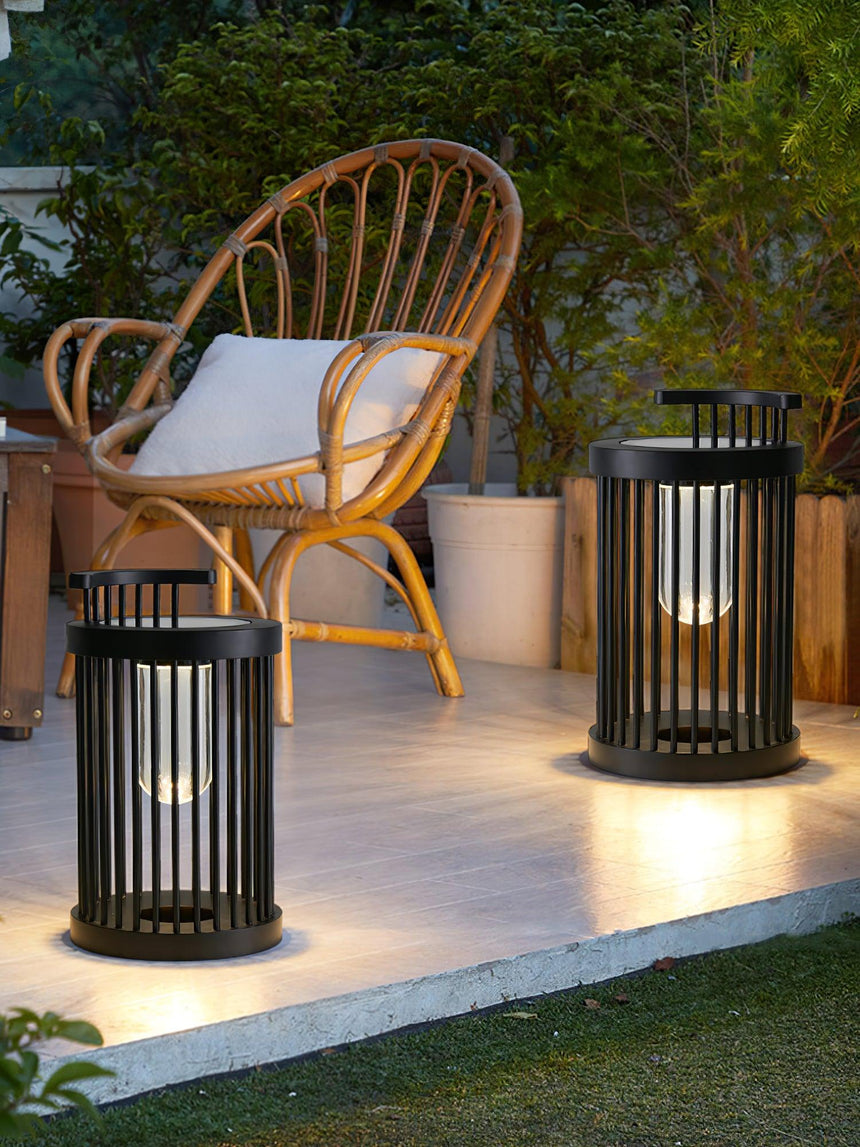 Two lanterns lit on paving beside a rattan chair at the edge of a lawn