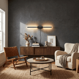 Black bar lit on a dark plaster wall above a console with a framed print and books