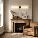Black bar lit above a wood mantel beside a leather armchair and a stack of books
