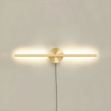 The taller gold profile lit on a pale wall, the cord dropping below the plate