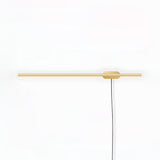 Slim gold bar crossing a round plate with a braided cord dropping down the wall