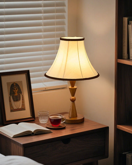 Cream shaded table lamp lit on a wooden bedside table beside a framed photo