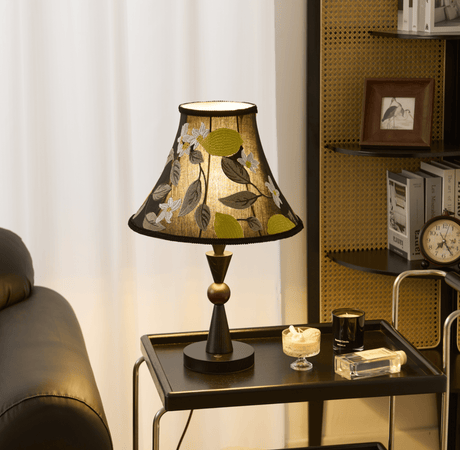 Black table lamp lit on a trolley beside a leather sofa and a shelf