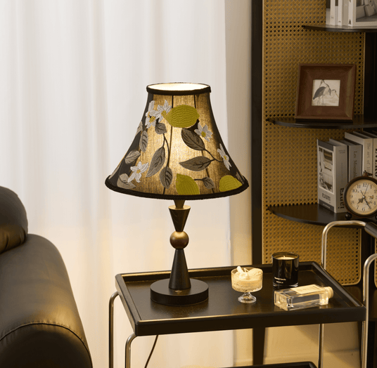Black table lamp lit on a trolley beside a leather sofa and a shelf