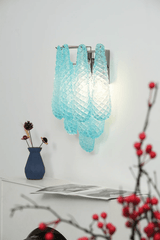 The blue sconce lit above a white shelf with a vase of red berries