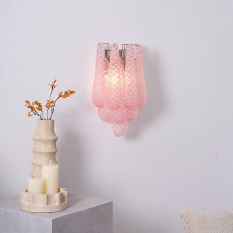 The pink sconce lit above a side table with candles and a vase