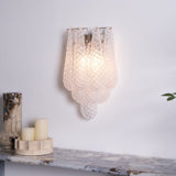 The clear sconce lit warm above a stone shelf with candles