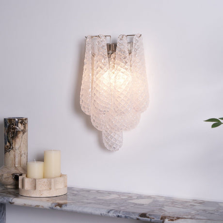 The clear sconce lit warm above a stone shelf with candles