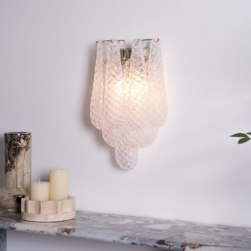 The clear sconce lit warm above a stone shelf with candles