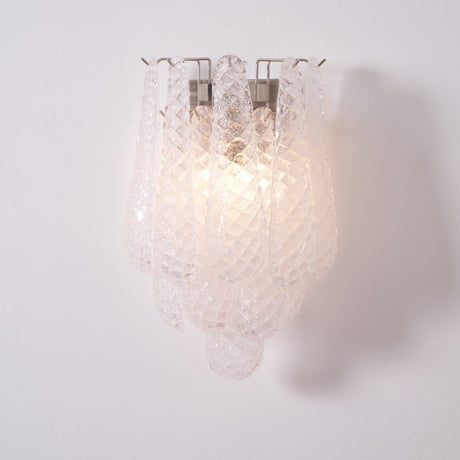 The clear sconce lit, the glass petals catching the light