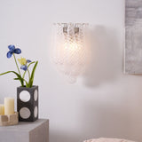 The clear sconce lit above a table with a vase of blue irises