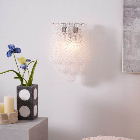 The clear sconce lit above a table with a vase of blue irises