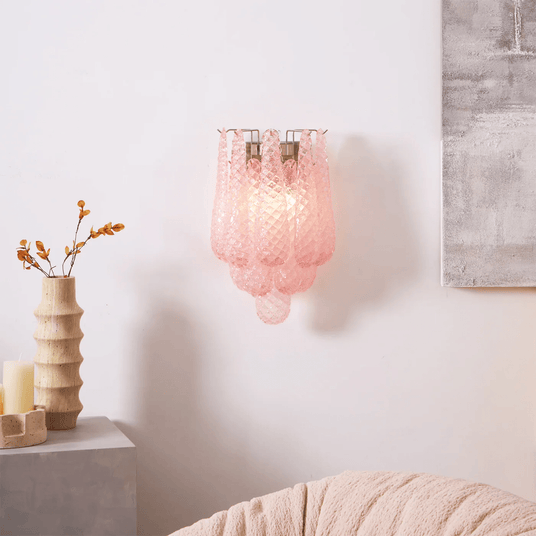 The pink sconce lit above a side table with a ribbed vase and dried branches