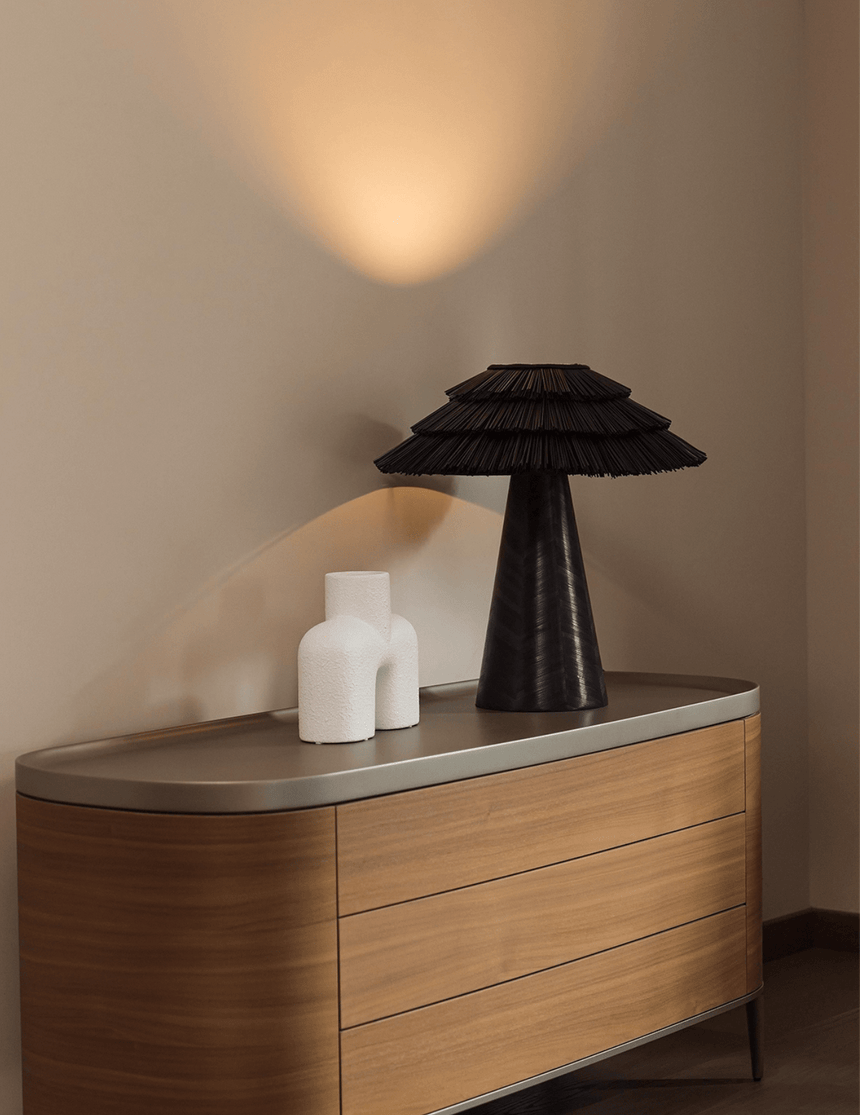 Black boho table lamp on a wooden sideboard beside pale candles