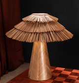 Boho table lamp seen close against a dark wall, straw tiers visible