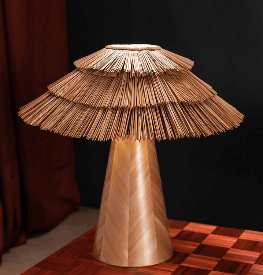 Boho table lamp seen close against a dark wall, straw tiers visible