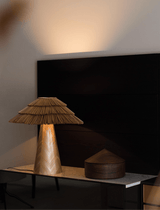 Boho table lamp lit on a dark console below a wall mounted screen