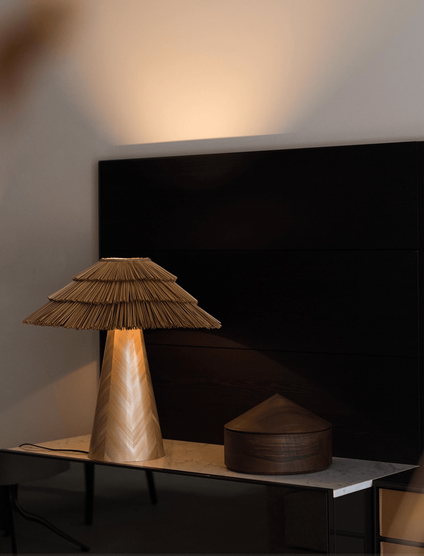 Boho table lamp lit on a dark console below a wall mounted screen