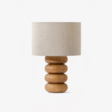 Table lamp with three stacked flattened wood spheres and a linen drum shade
