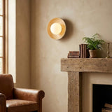 The bowl sconce lit above a rustic wood mantel beside a leather armchair