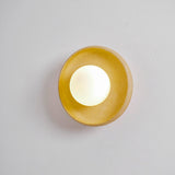 The round sconce lit on a pale wall, the glaze turning warm gold