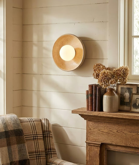 The sconce on a white shiplap wall above a mantel with dried flowers and a plaid chair