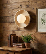 The sconce glowing on a reclaimed wood wall above a side table with books and a fern