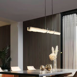 The glass branch lit above a dining table against a dark ribbed wall