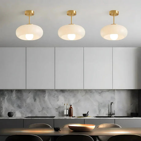 Three white glass domes on brass stems lit above a dark kitchen counter