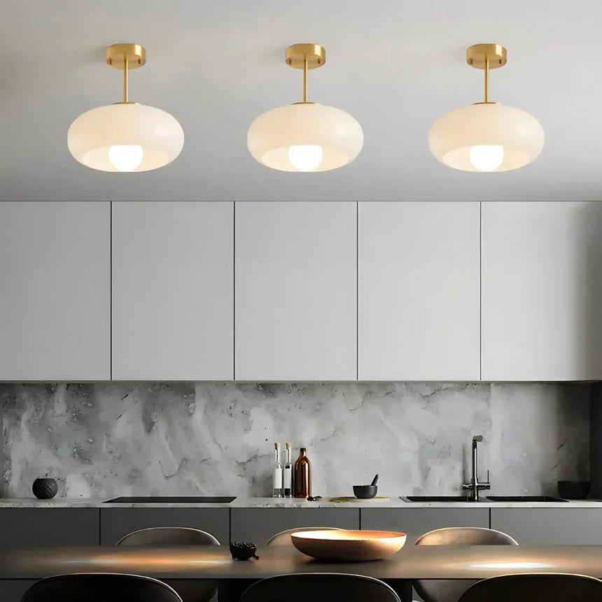 Three white glass domes on brass stems lit above a dark kitchen counter