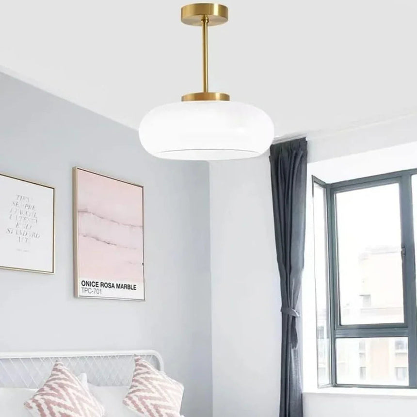 The white glass dome lit near a window above a bed with cushions
