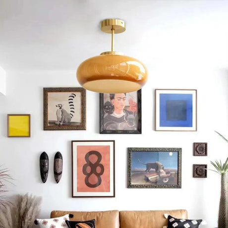 The yellow glass dome on a brass stem lit above a sofa and a gallery wall