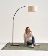 Black arc lamp on a green rug, a woman seated under the shade reading