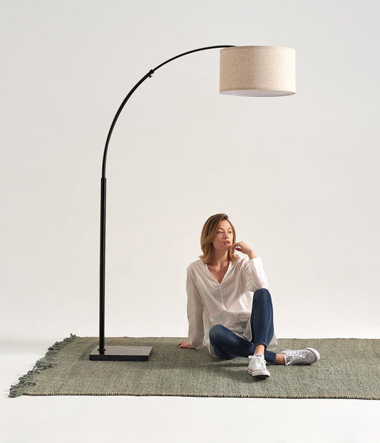 Black arc lamp on a green rug, a woman seated under the shade reading