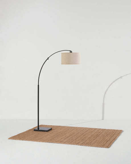 Black arc lamp on a woven rug, the base set behind the line of the shade