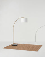 Brass arc lamp standing on a woven rug, the shade tipped over the floor