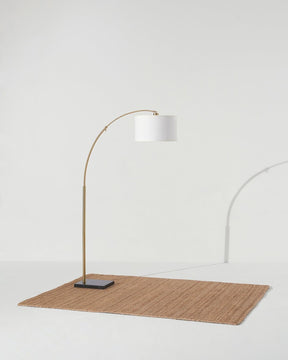 Brass arc lamp standing on a woven rug, the shade tipped over the floor