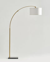 Brass arc floor lamp with a white drum shade on a dark rectangular base