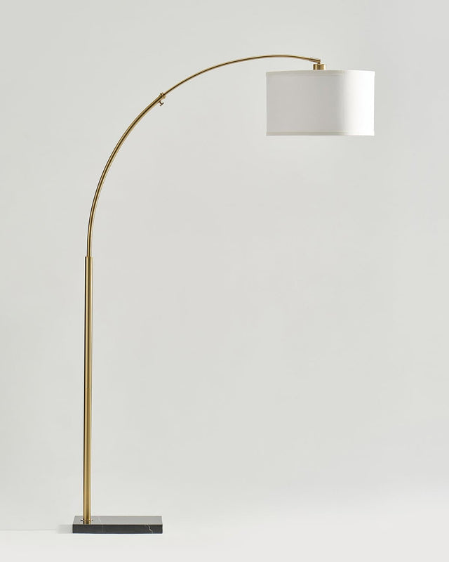 Brass arc floor lamp with a white drum shade on a dark rectangular base
