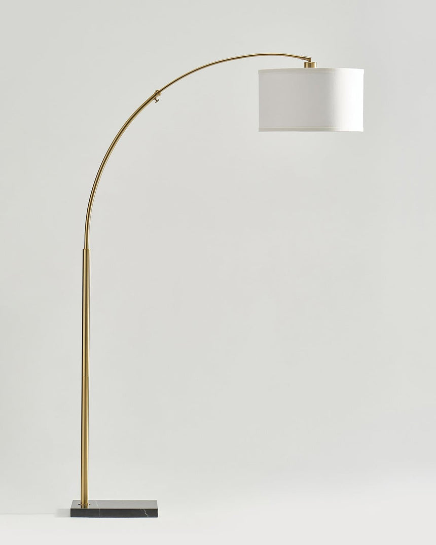 Brass arc floor lamp with a white drum shade on a dark rectangular base