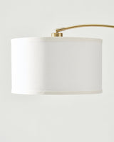 The brass arm entering the top of the white drum shade at a fixed collar