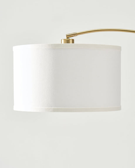 The brass arm entering the top of the white drum shade at a fixed collar