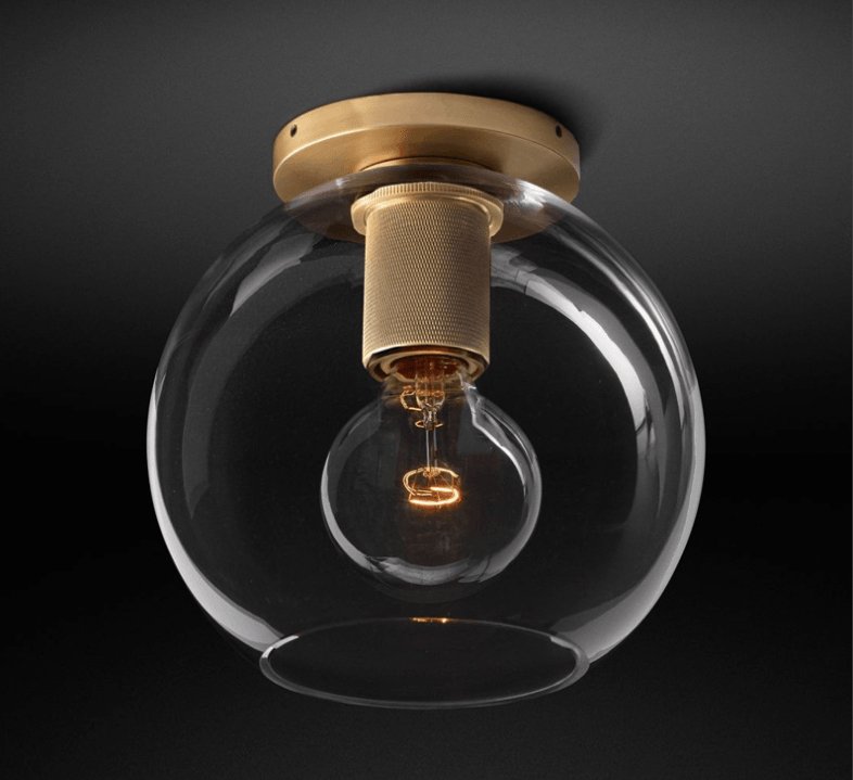 Brass ceiling light with a clear globe shade seen against a dark backdrop