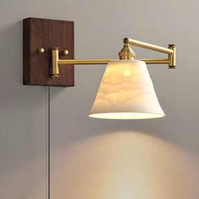 Ceramic bell shade lit on a brass arm over a walnut plate, cord below