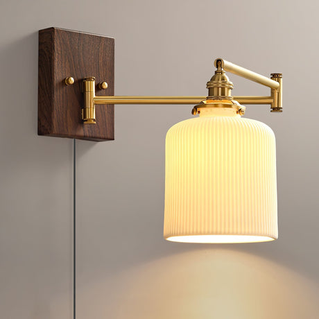 Ribbed ceramic drum shade lit warm on a brass arm and walnut plate